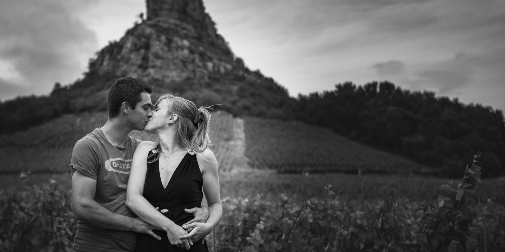 Portrait d'un couple qui s'embrasse, réalisé en été dans les vignes à roche Solutré pour une séance d'engagement à Mâcon