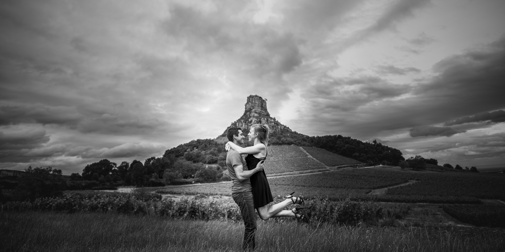 Photo d'un couple heureux, réalisé en été dans les vignes à roche Solutré pour une séance d'engagement à Mâcon